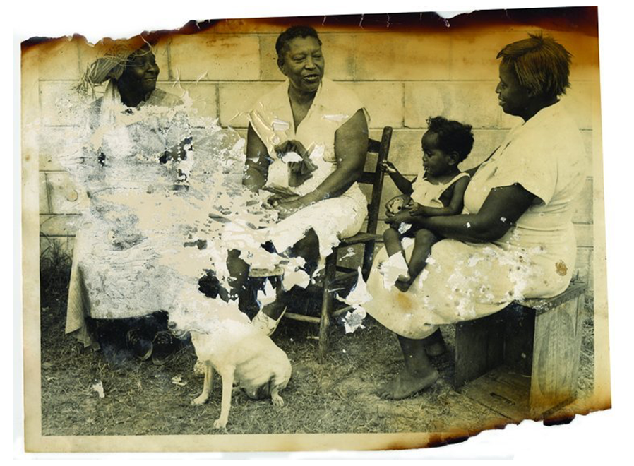 A partly burned, yellowed photograph of three black women sitting in chairs, one holds a young child on her lap