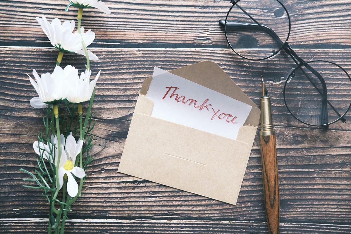 A “Thank you” note in an envelope with flowers, a pen and spectacles. A “Thank you” note in an envelope with flowers, a pen and spectacles.