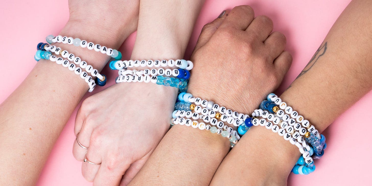 Four people's forearms lay across a pink background. Each is wearing friendship bracelets with letter beads - though they feature unusual text related to Wirecutter article rankings.