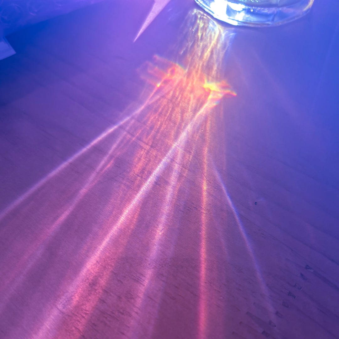 A purple-tinted photo of light shining through a glass of water onto a wooden tabletop.