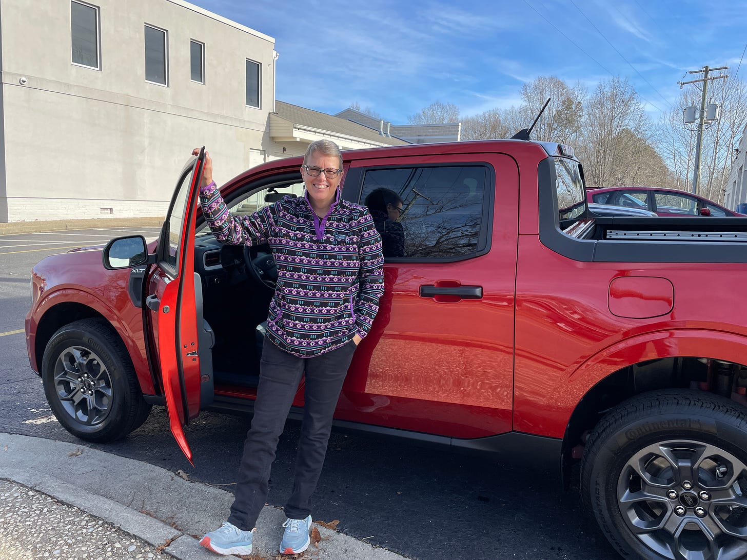 A woman with short hair and glasses standing next to her Wendy and her “hot-pepper red” 2024 Ford Maverick hybrid. 