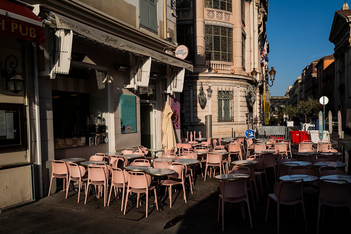 	Empty Café Tables in Morning Light – Rows of pink café chairs and tables sit empty outside a restaurant in Nice, bathed in the warm morning sun, awaiting the first customers of the day.