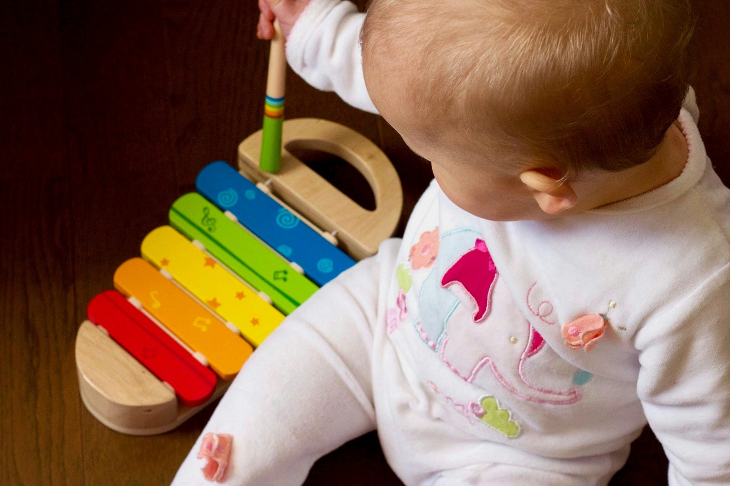 Una bambina di quattro o cinque mesi, seduta a terra, gioca con uno xilofono di legno colorato