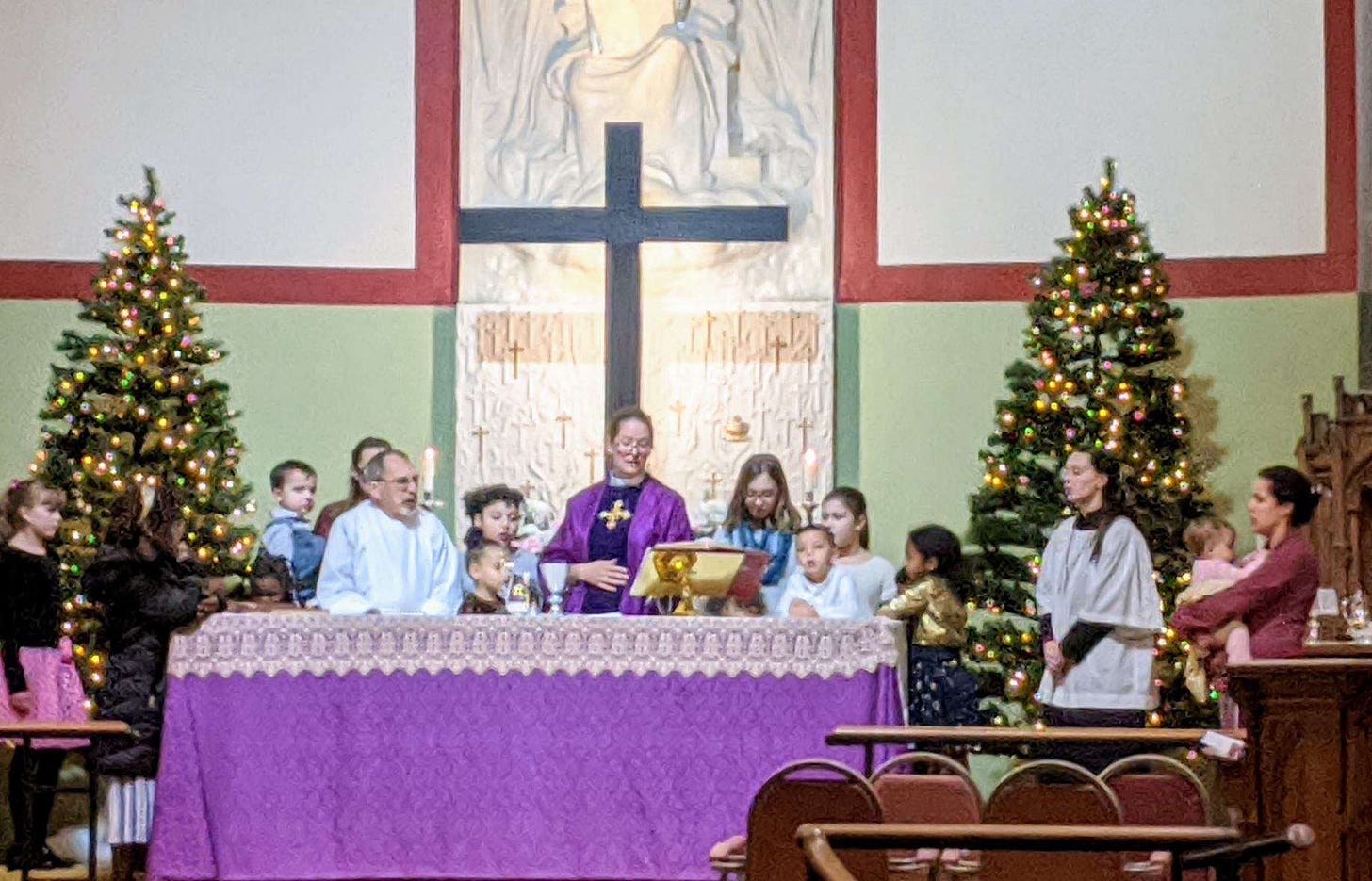 Children gather around an altar prepared in purple for Advent as the priest leads the Eucharist liturgy