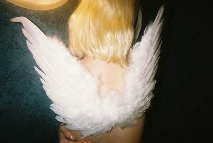 This may contain: a woman with long blonde hair and white angel wings on her back, next to a clock