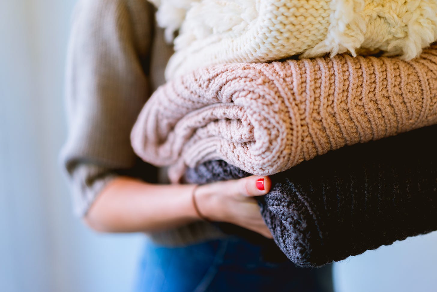 Woman holding a pile of folded sweaters in different colors