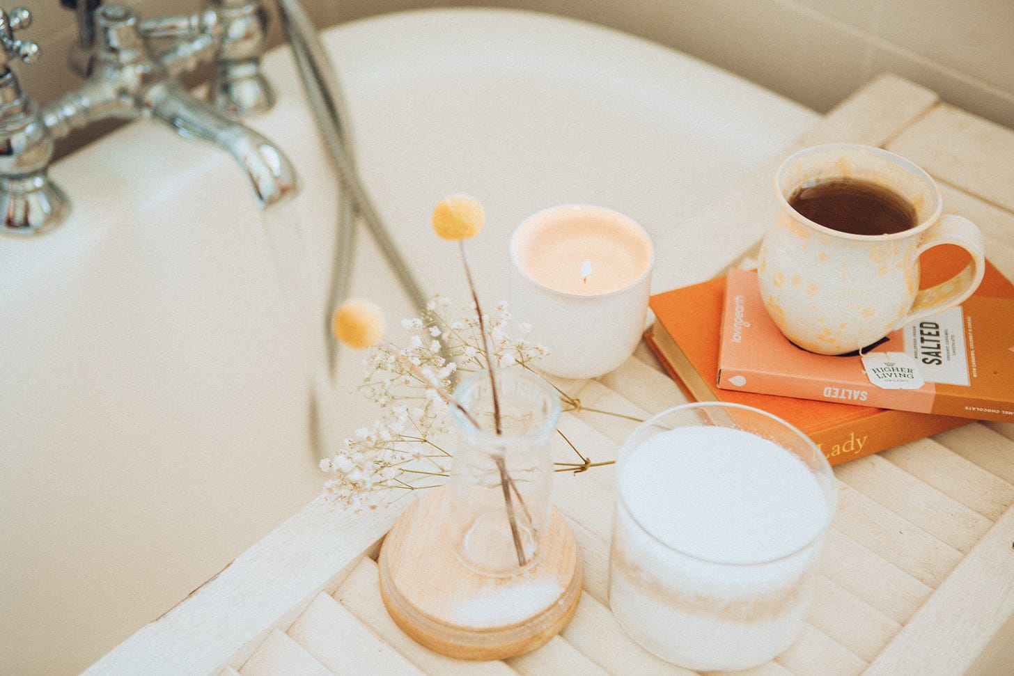 bath setting with orange coloured books and pastel flowers and candles