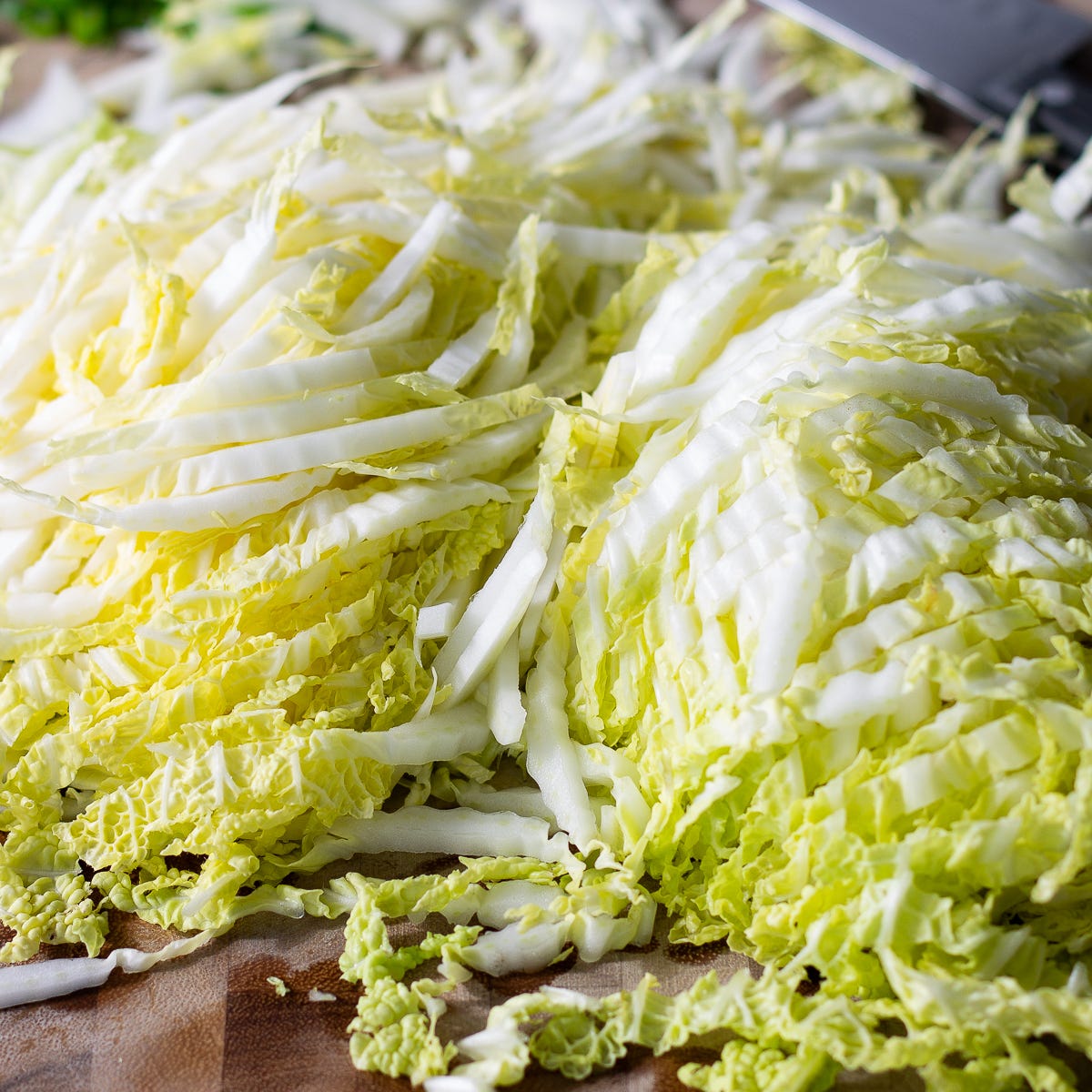 A head of Napa cabbage that has been sliced thin on a cutting board. 