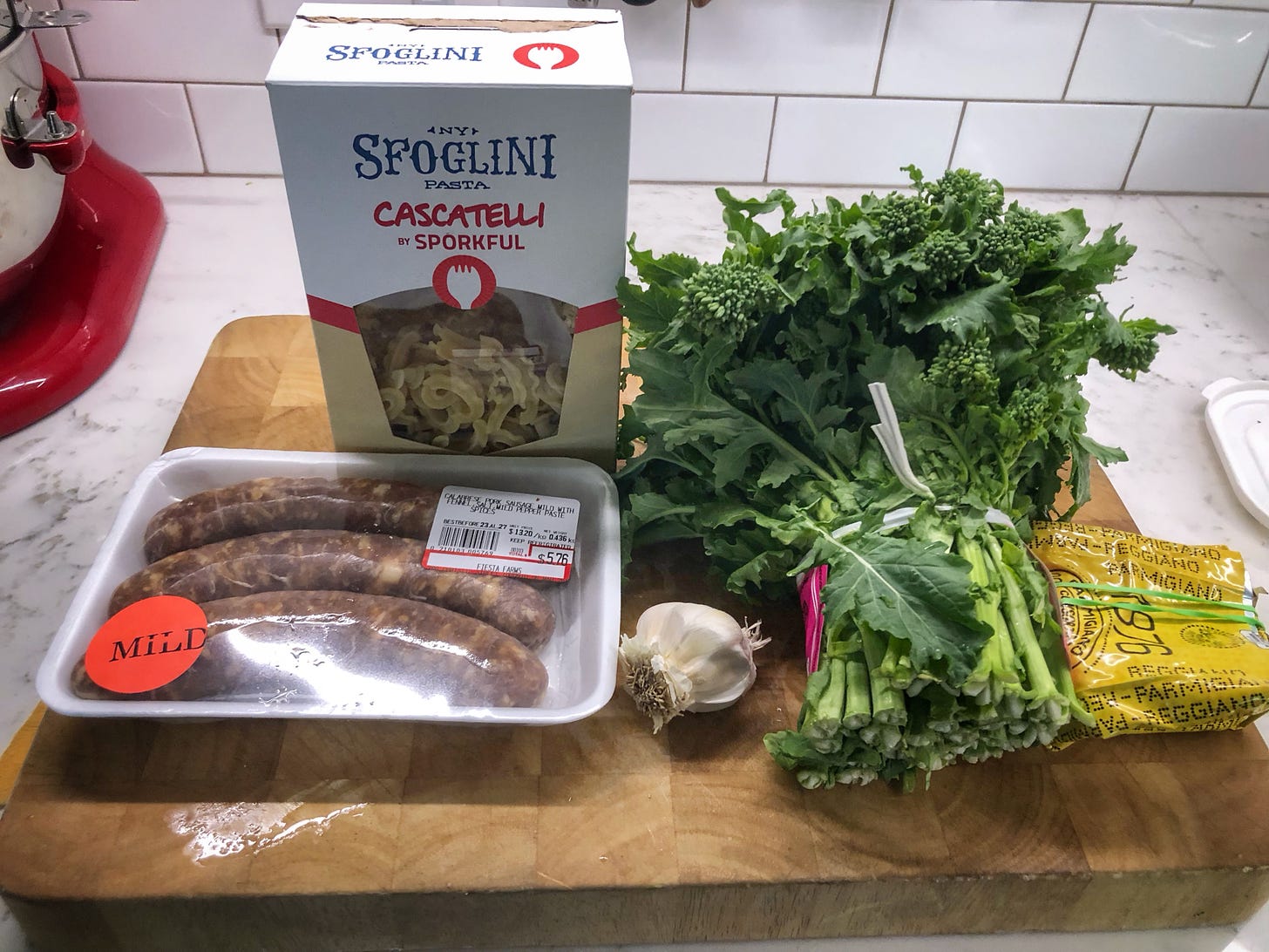 The ingredients for the recipe: cascatelli pasta, Italian sausage, rapini, garlic, and Parmesan cheese, arranged on a counter