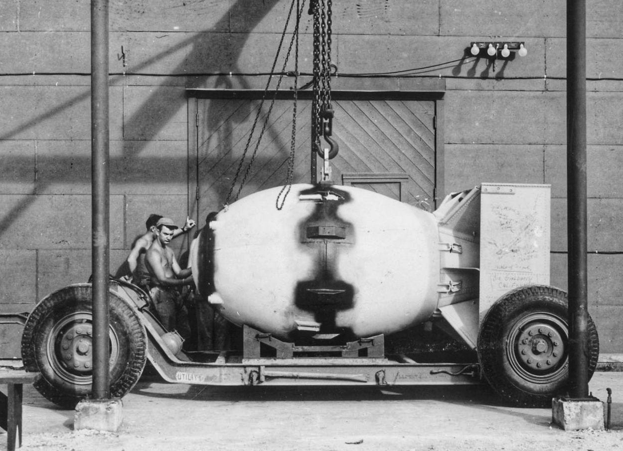 Titelbild, Schwarz-Weiß-Foto, 1945: Atombombe (Deckname "Fat Man") auf einem Anhänger vor einer Wartungshalle. Links neben der Bombe stehen zwei Soldaten mit nacktem Oberkörper.