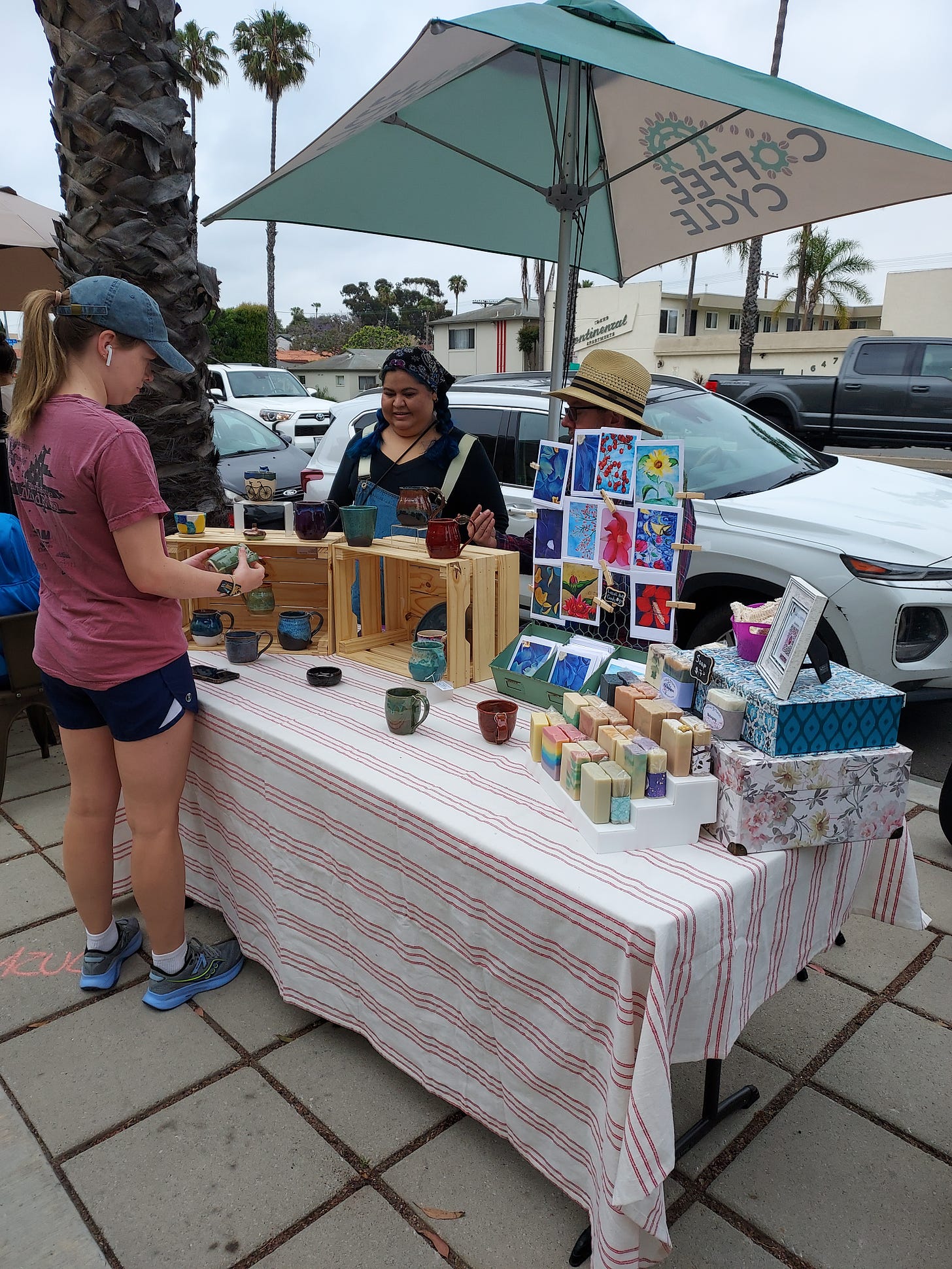 A jogger stops to admire handmade clay mugs and homemade soaps at a makers market on a SoCal sidewalk.