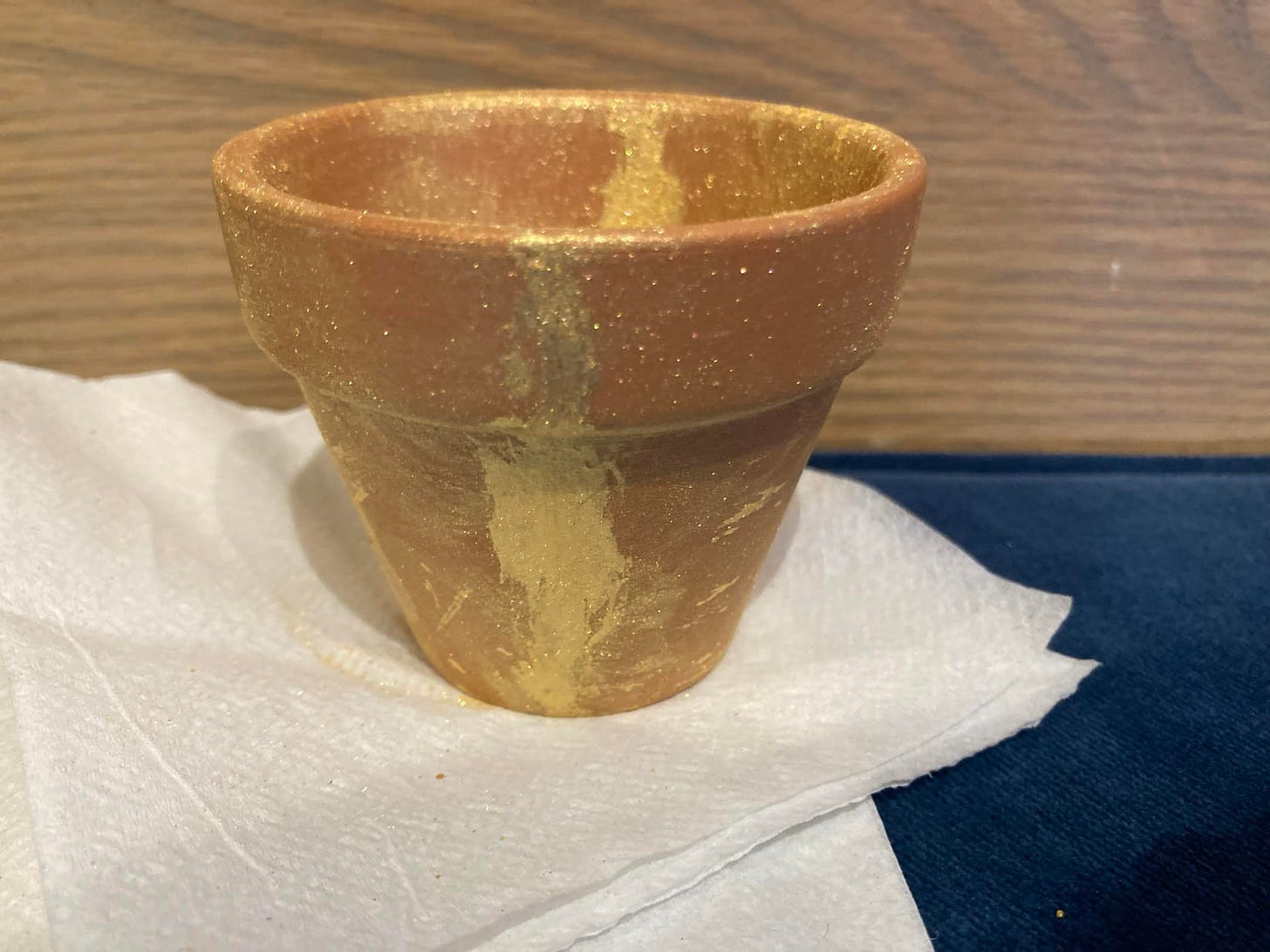 A flower pot smudged with gold, sparkling paint on a paper towel