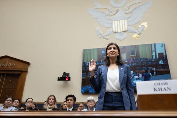 Lina Kahn, wearing a blue blazer and white blouse, raises her right hand as she is sworn in at hearing.