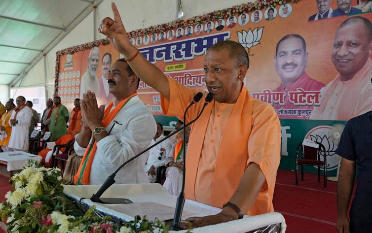A man in saffron shirt speaks into a microphone as several other people stand next to him