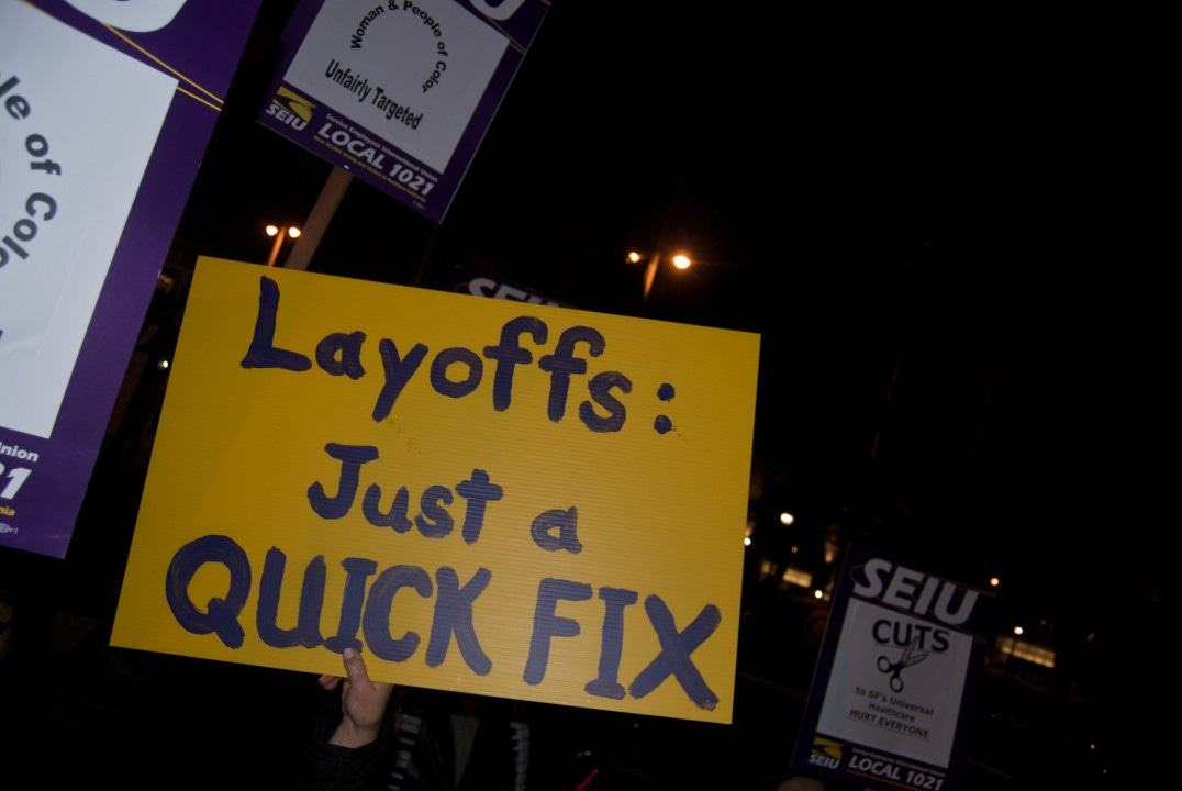 Strikers holding union signs and a sign saying, "Layoffs: Just a QUICK FIX"