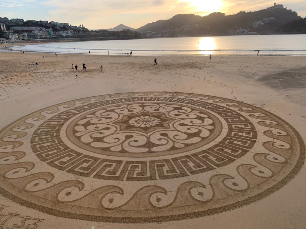 A very large mandala in the sand on the beach at sunset.