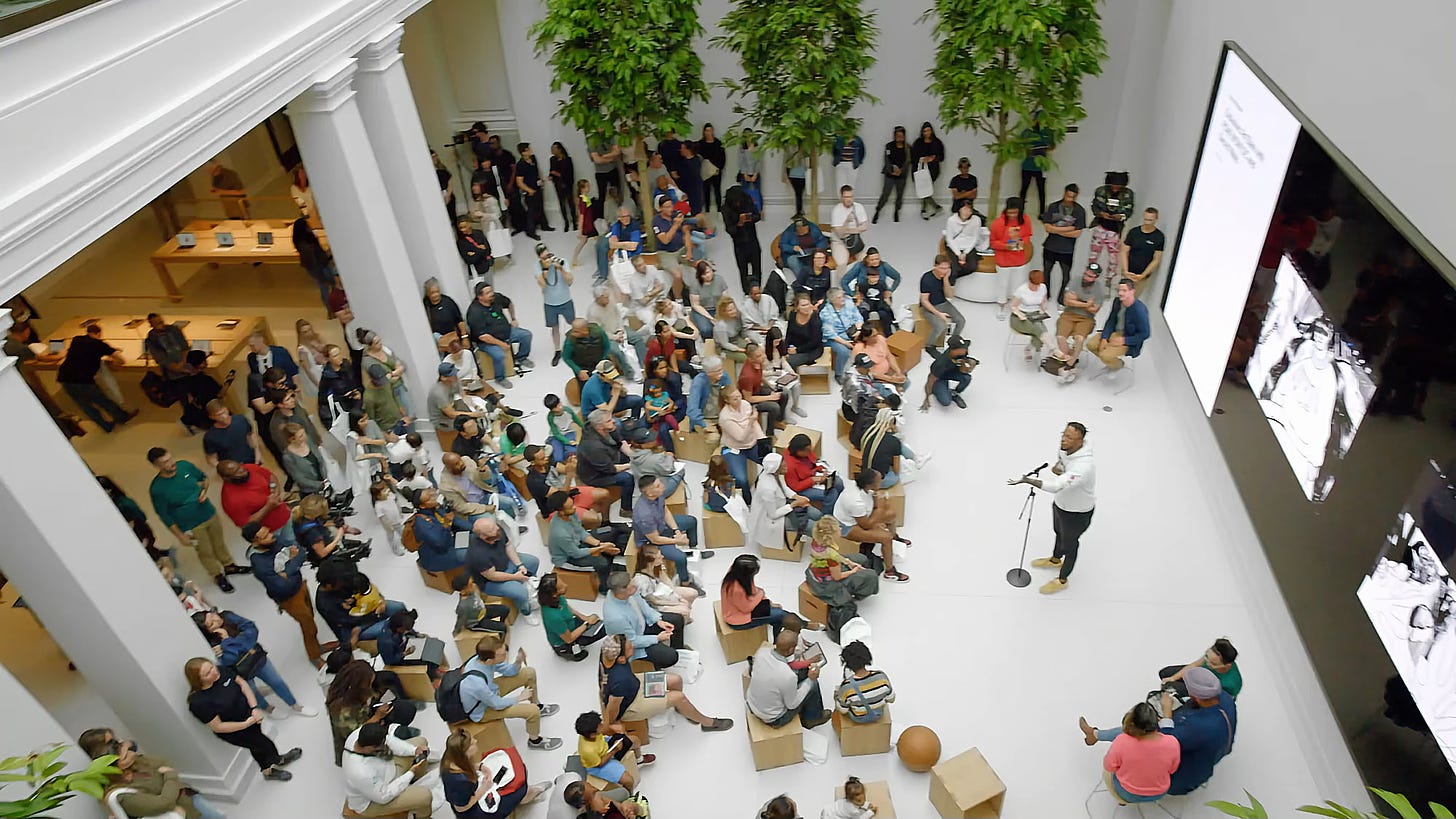 A Today at Apple performance during the grand opening of Apple Carnegie Library. The photo was taken from the balcony above the Forum, which is filled with people. This article's author is seated near the bottom left of the frame.