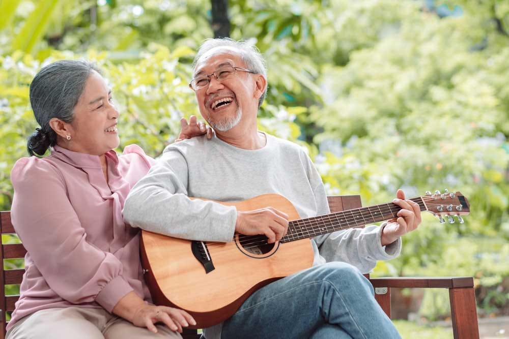 Elders enjoying learning the guitar while sitting outdoors.