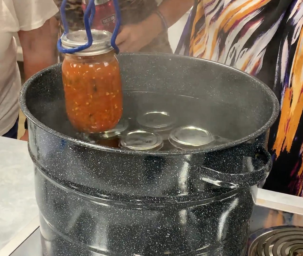 A jar of salsa being put into a water bath canner