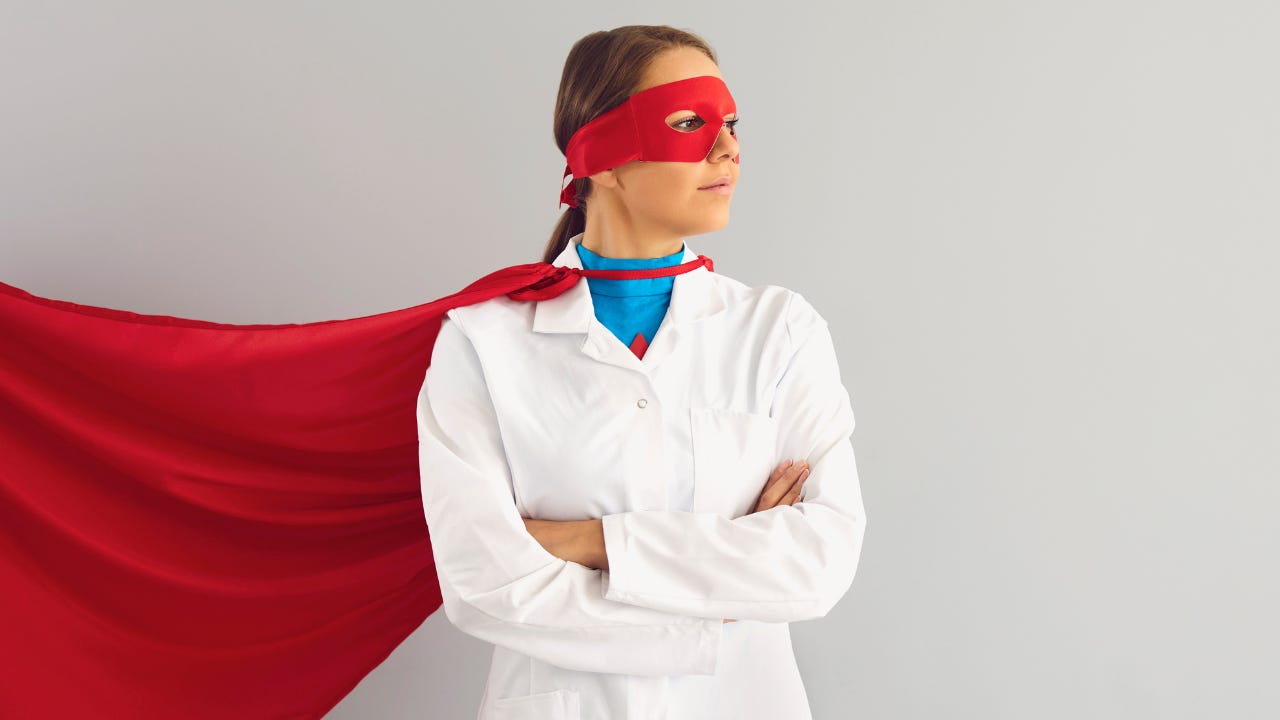 A woman wearing a white coat, a red mask, and a red superhero cape.
