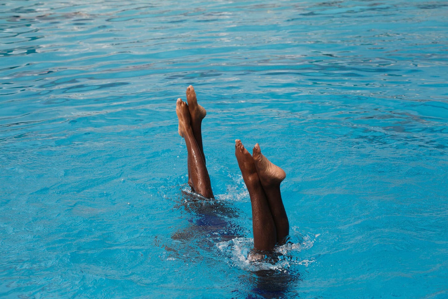 An image of two pairs of brown pointed feet emerging from blue water.