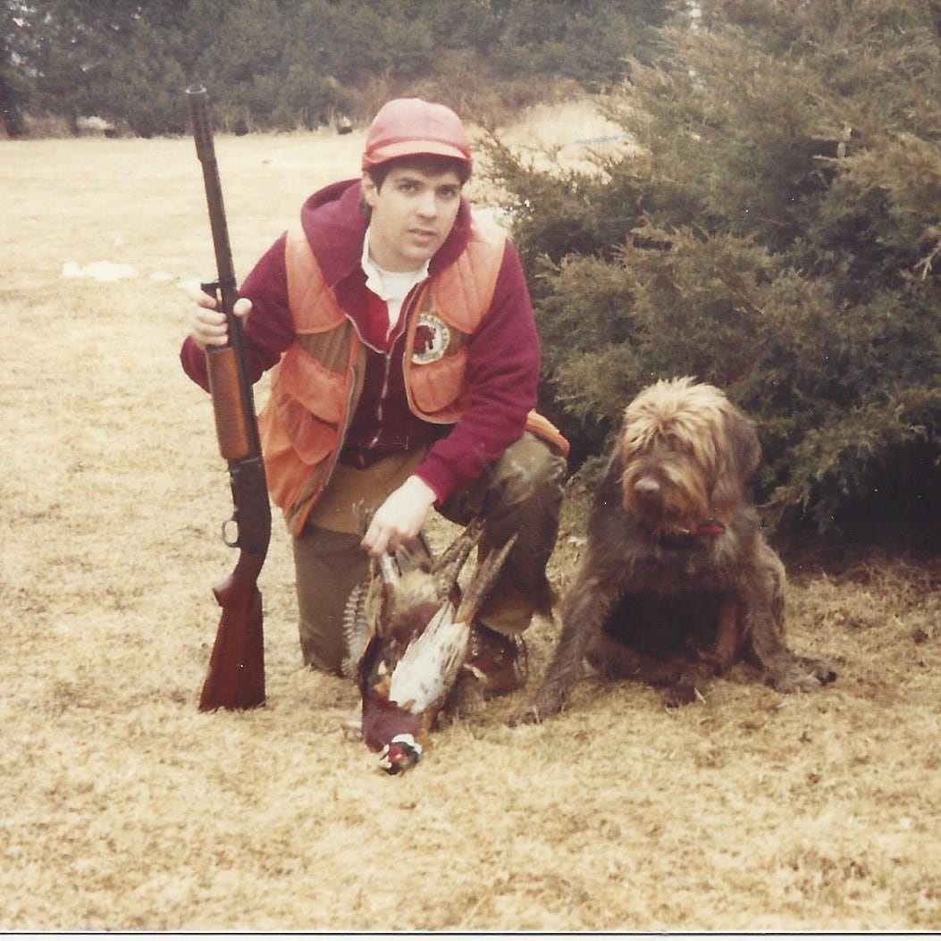 A 20-something hunter with a rifle posed next to a dog and pheasants