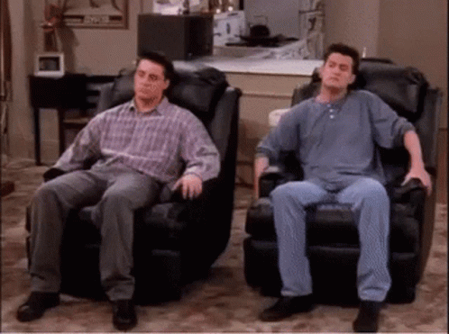 GIF from the show Friends with Chandler and Joey taking out their comfy leather chairs in front of the TV.