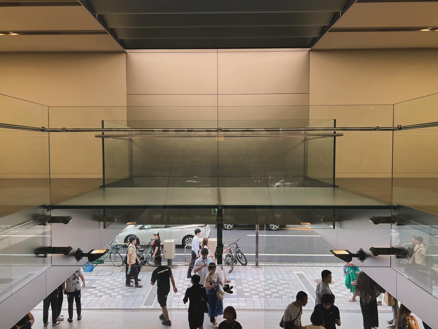 The upper level glass bridge and street entrance to Apple Nagoya Sakae as viewed from the staircase in the center of the store.