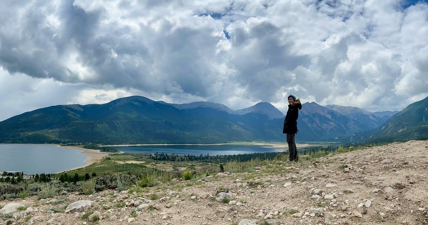 Lyric, standing on top of one mountain, above two lakes, viewing the other mountains and could. 