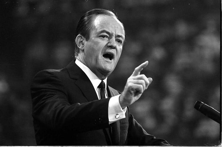 A man in a suit and tie, speaking to a crowd.