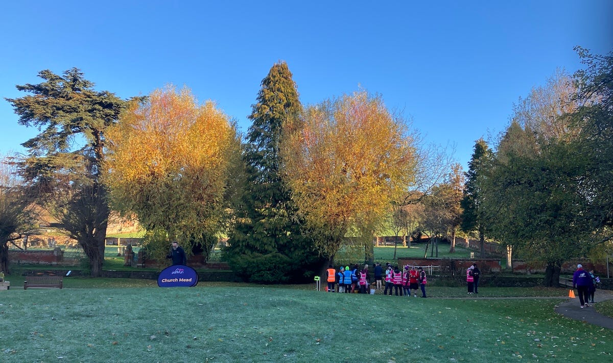 People gathered at the start of the parkrun under blue skies and orange-leaved trees