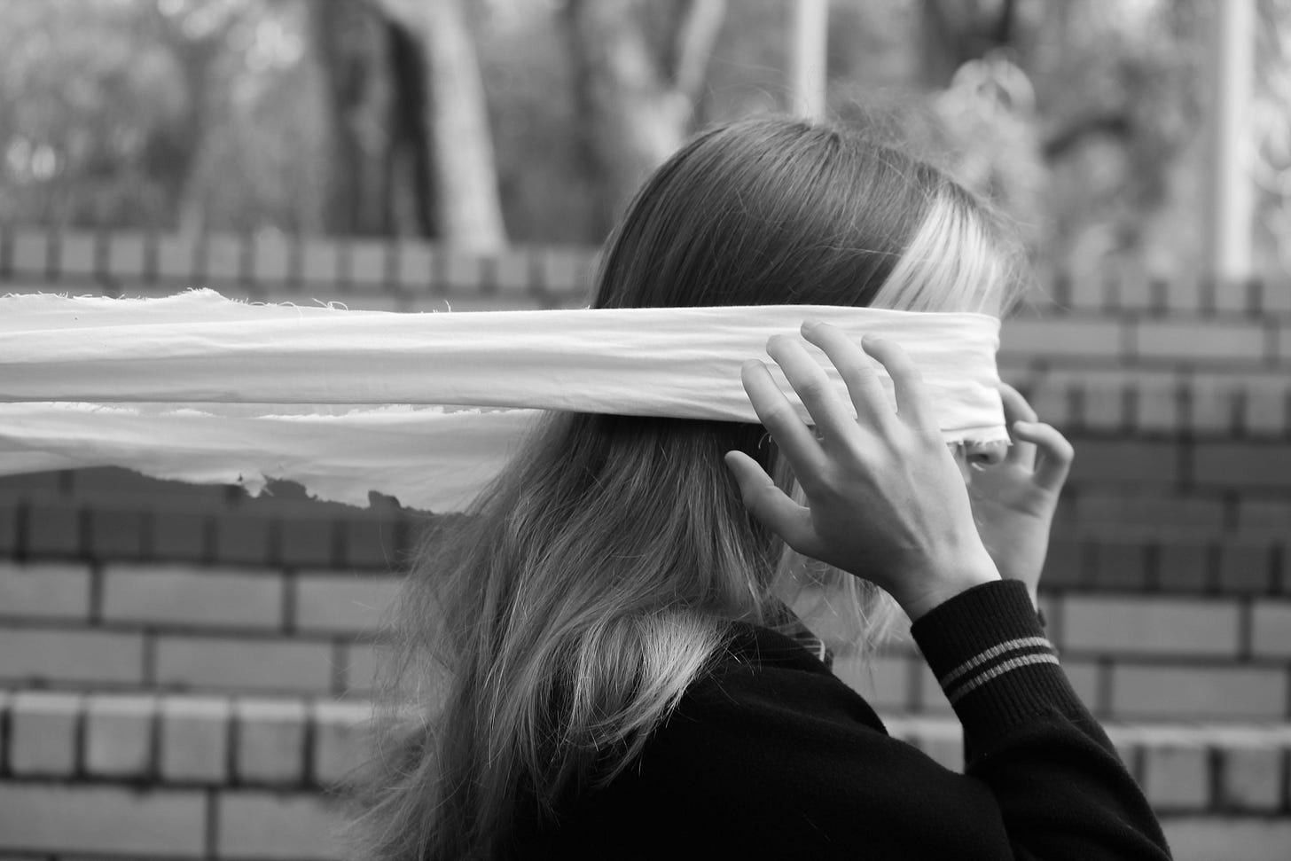 A long white blindfold stretches around a woman's eyes as she reaches for it.