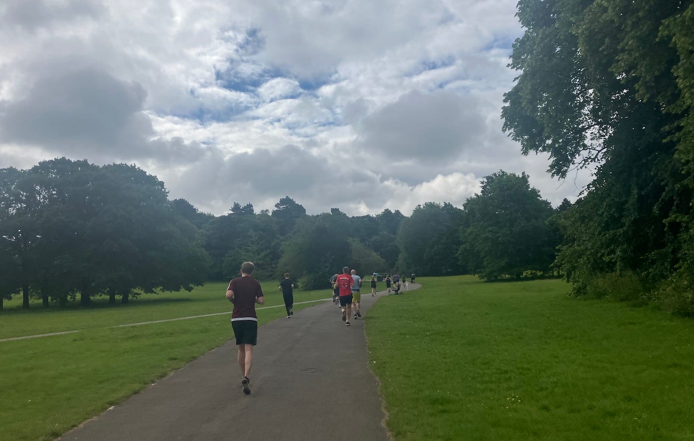 Runners on a path through green fields and trees