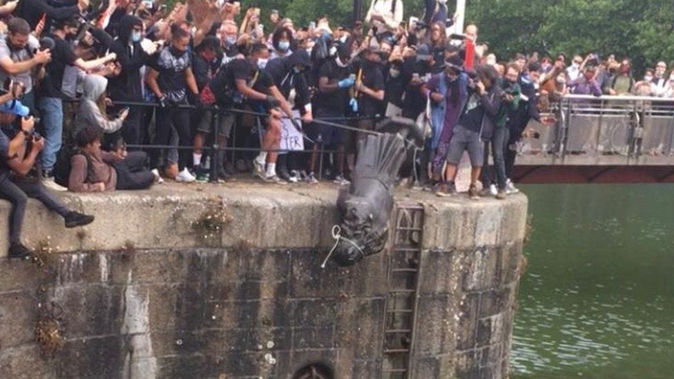 A crowd throwing a statue into a harbour