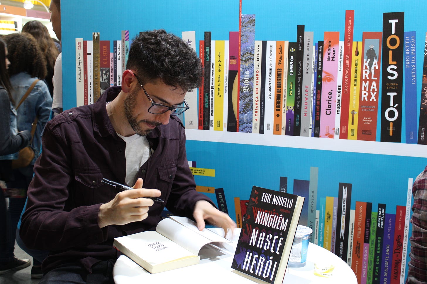 Sentado à uma mesa fora do estande de livros da Companhia das Letras autografando Ninguém Nasce Herói. 