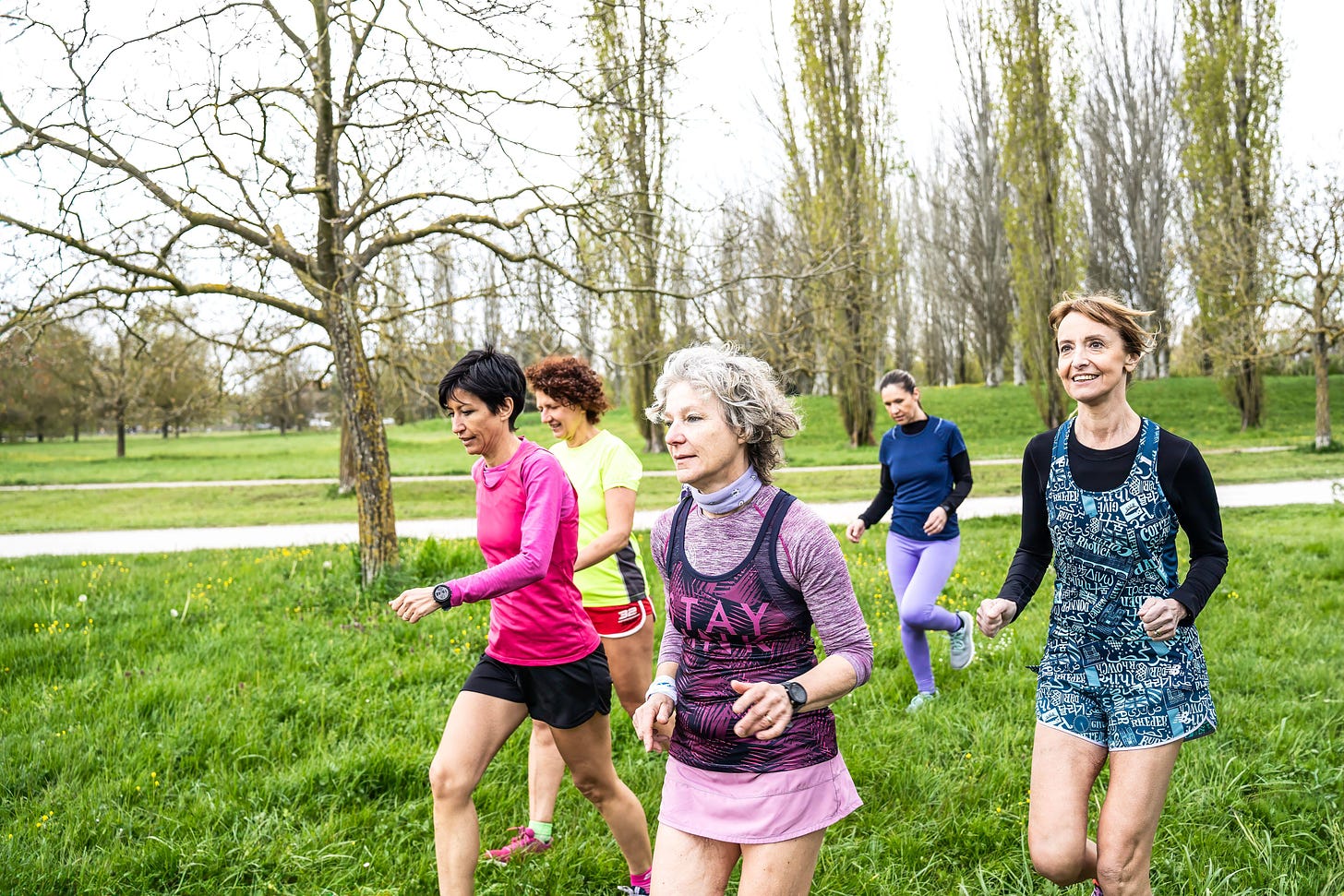  Group of middle-aged women in colorful sportswear jogging 