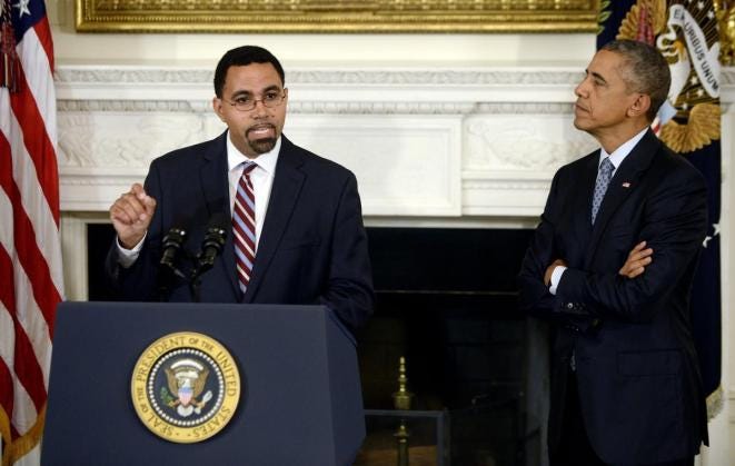 John B. King Jr., a Black man wearing glasses with a goatee, stands at a lectern next to President Obama.