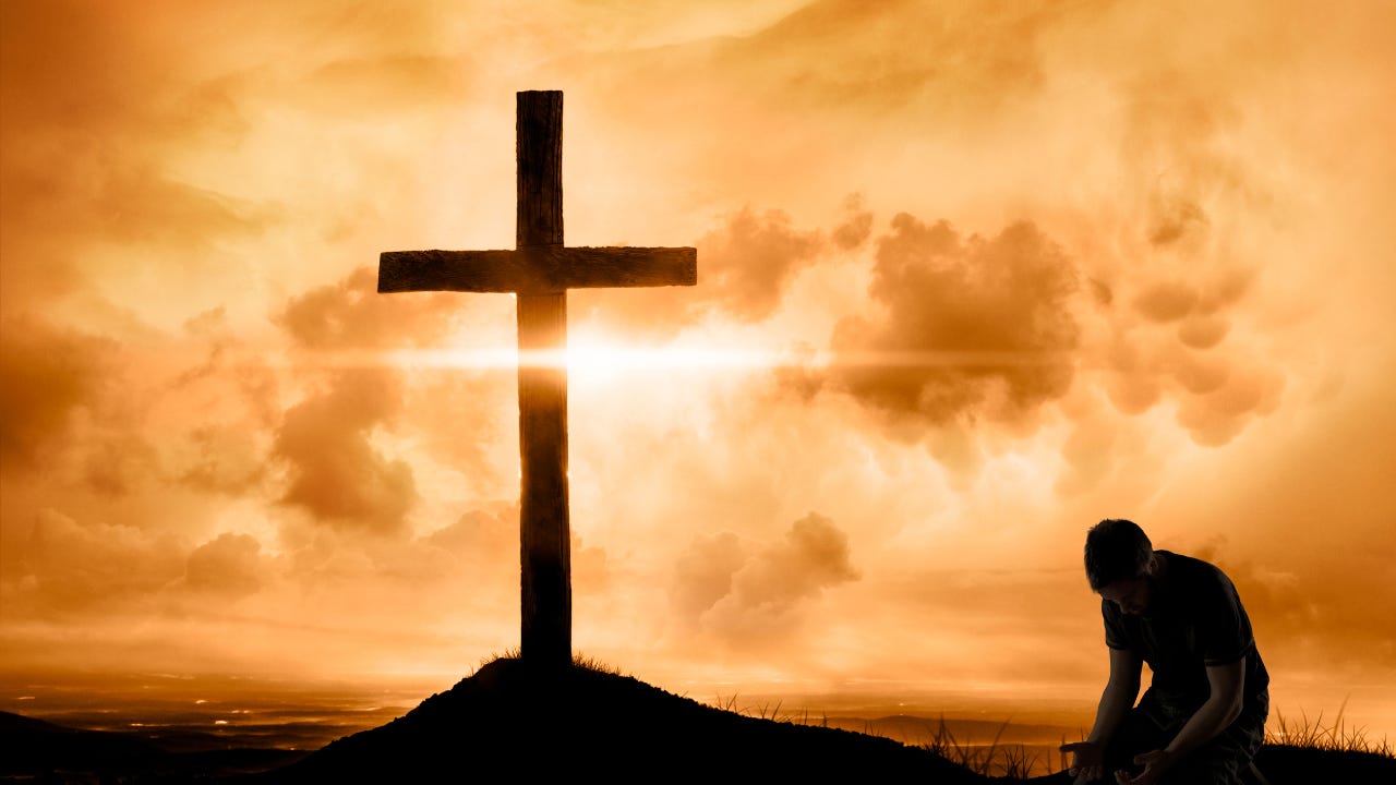 A man kneeling beside a wooden cross.