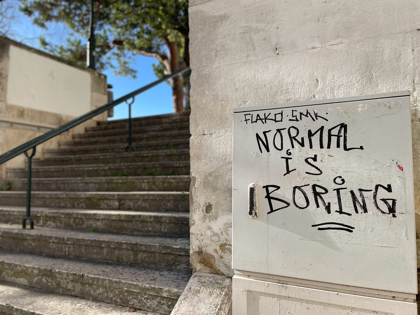 the words Normal is Boring are written on a wall in Lisbon, Portugal