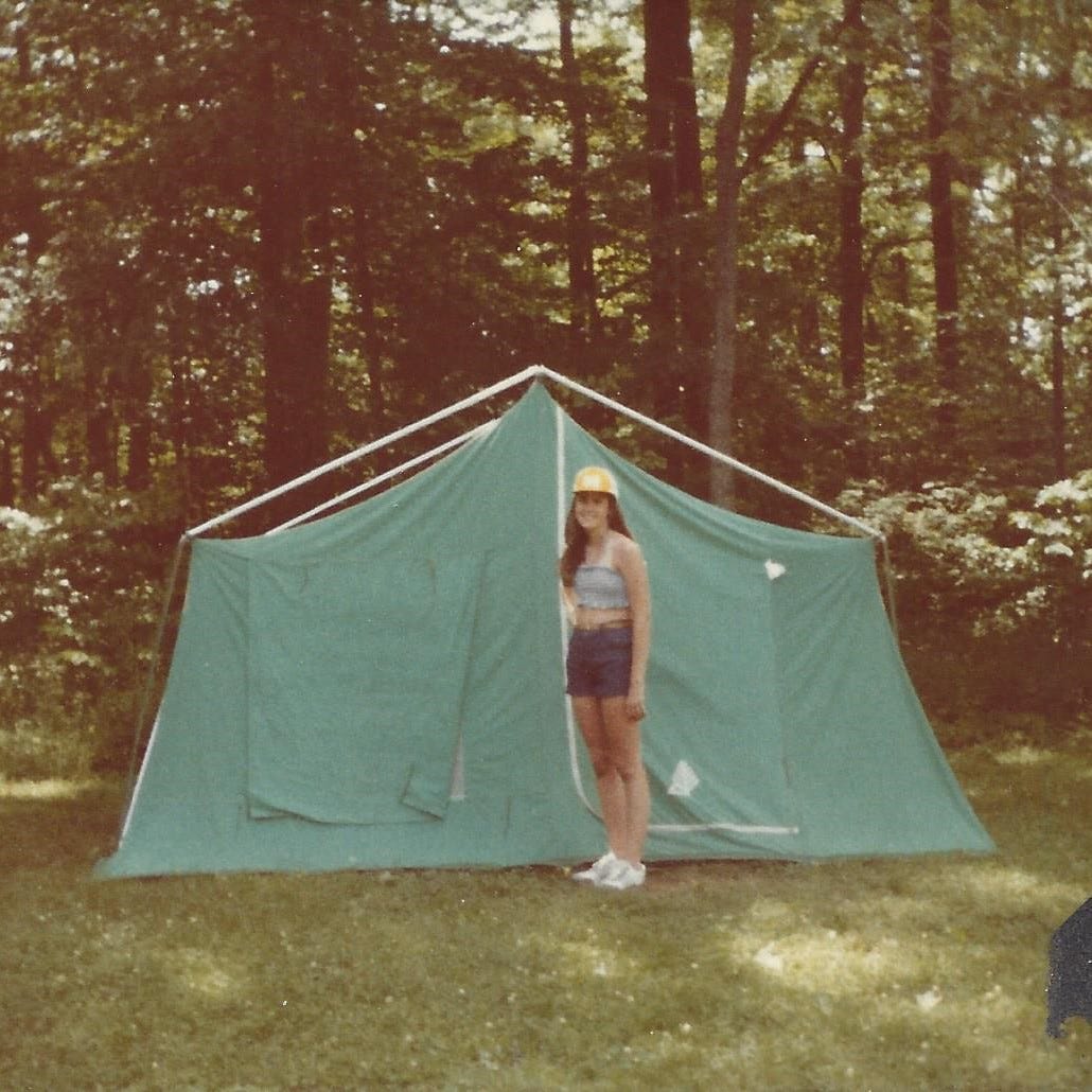 15-year-old girl stands proudly outside the tent she pitched at a campground