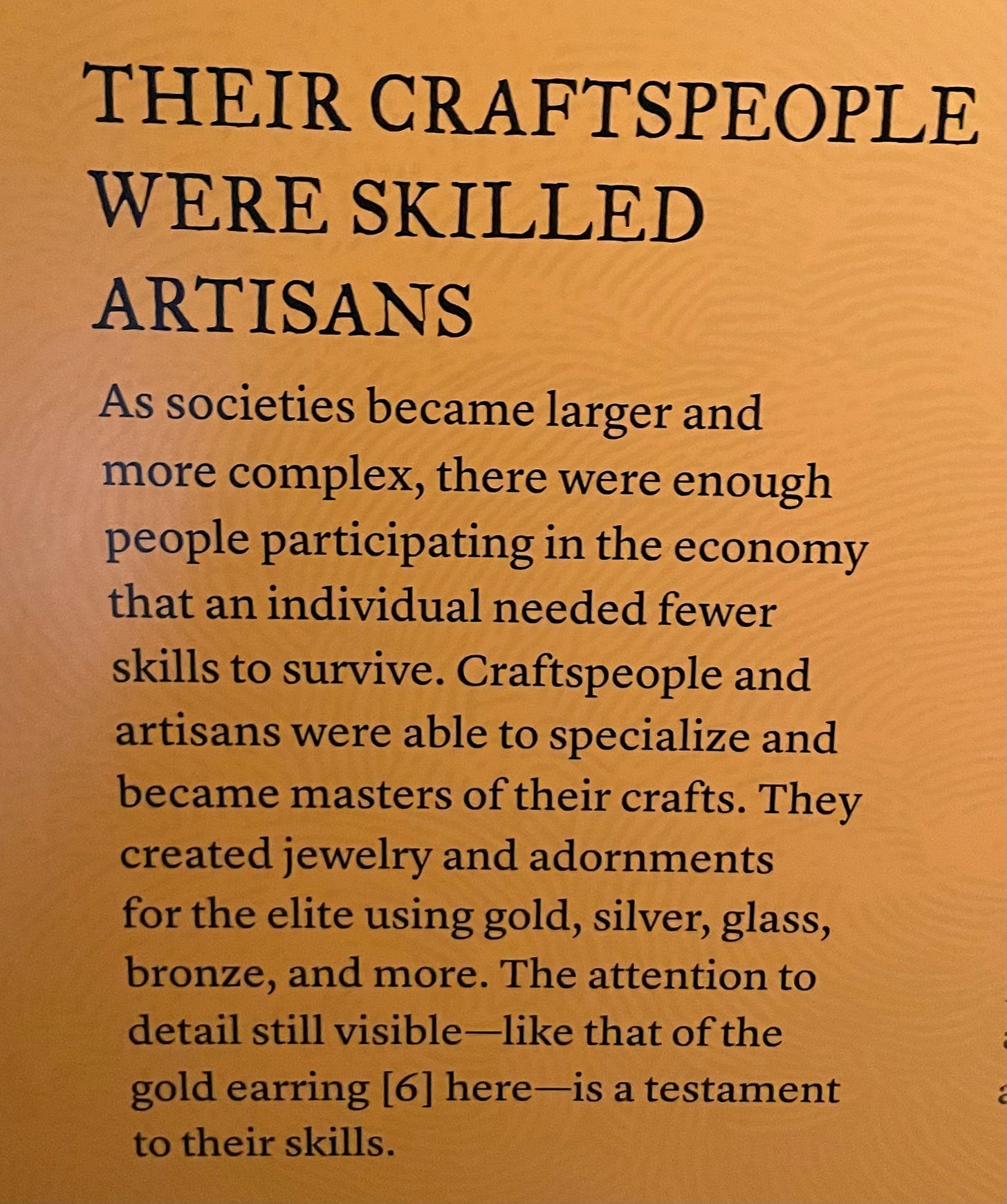 museum plaque reading 'their craftspeople were skilled artisans. As societies became larger and more complex, there were enough people participating in the economy that an individual needed fewer skills to survive. Craftspeople and artisans were able to specialize and became masters of their crafts. They created jewelry and adornments for the elite using gold, silver, glass, bronzes, and more.