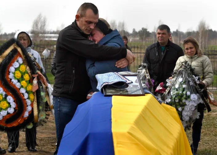 Two family members embrace near a coffin, draped in the colors of Ukraine, holding the remains of Bogdan Volodymerovuch Tromssa.