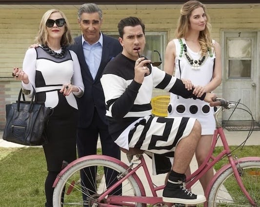 Photo of a wealthy family, posed together in front of an old house. They are wearing ridiculous fancy clothes and the son is riding a pink bike in the front.