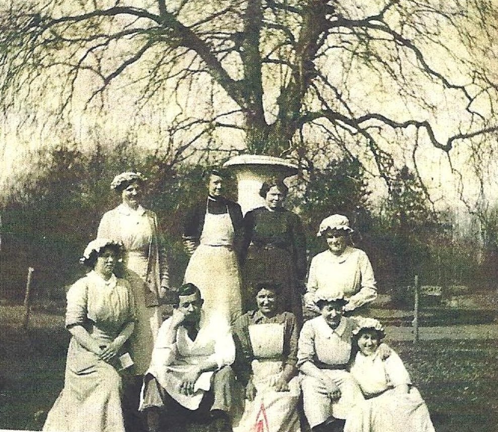 A black and white photograph of the kitchen staff in the park at Royaumont during WWI, sitting at the center are Chef Michelet and Jeanne Desbordes, among Scottish women.