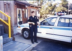 Female police officer in uniform standing next to white and blue police car