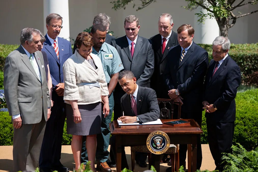President Barack Obama signing agricultural sustainability initiatives outdoors at a wooden desk, surrounded by several officials and community representatives, symbolizing a hopeful moment in climate-smart agricultural policy.