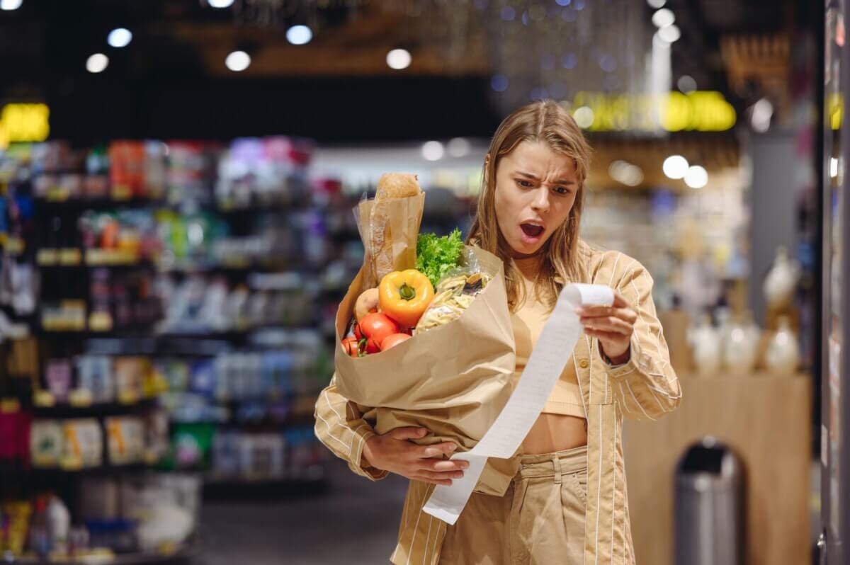 Young sad customer reads bill holding brown paper bag shopping at supermarket