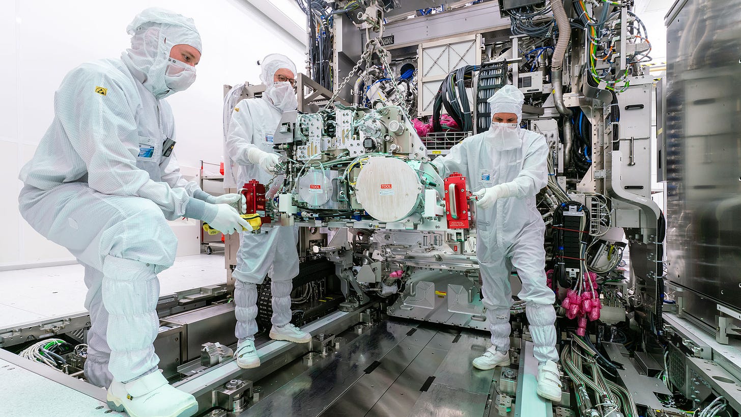 Three cleanroom engineers work on assembling an EUV system, moving the source into the body. 