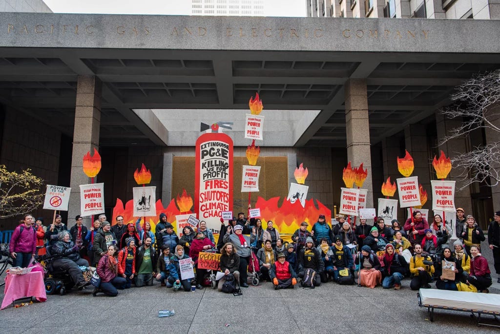 Reclaim Our Power rallies outside of PG&E’s San Francisco headquarters in December 2019. A group of organizers including wheelchair users pose for a photo with striking flame signs held above, making it look like the group is on fire.