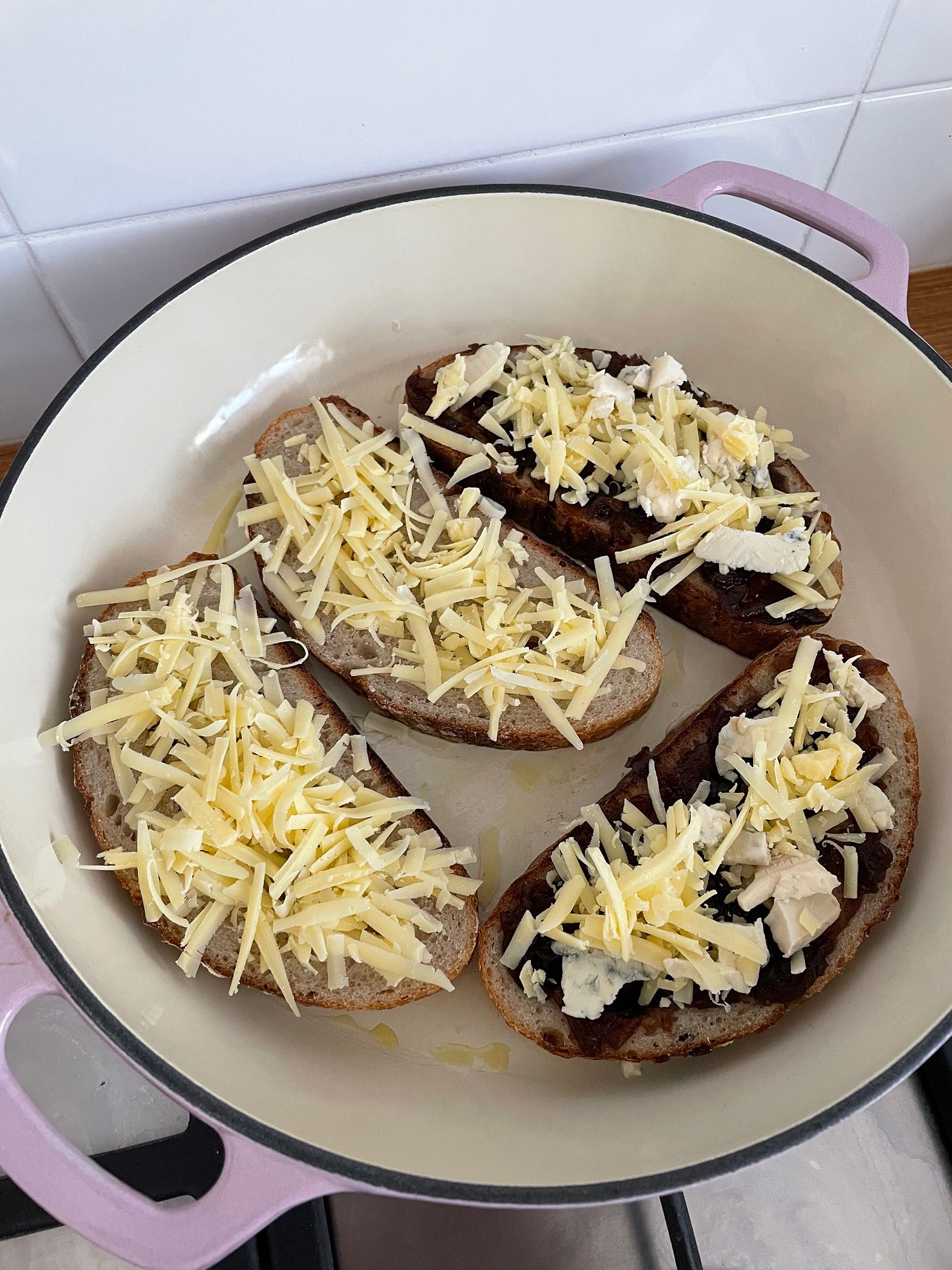 Shallow pan with four slices of bread topped with grated cheese, making caramelised onion and cheddar grilled cheese
